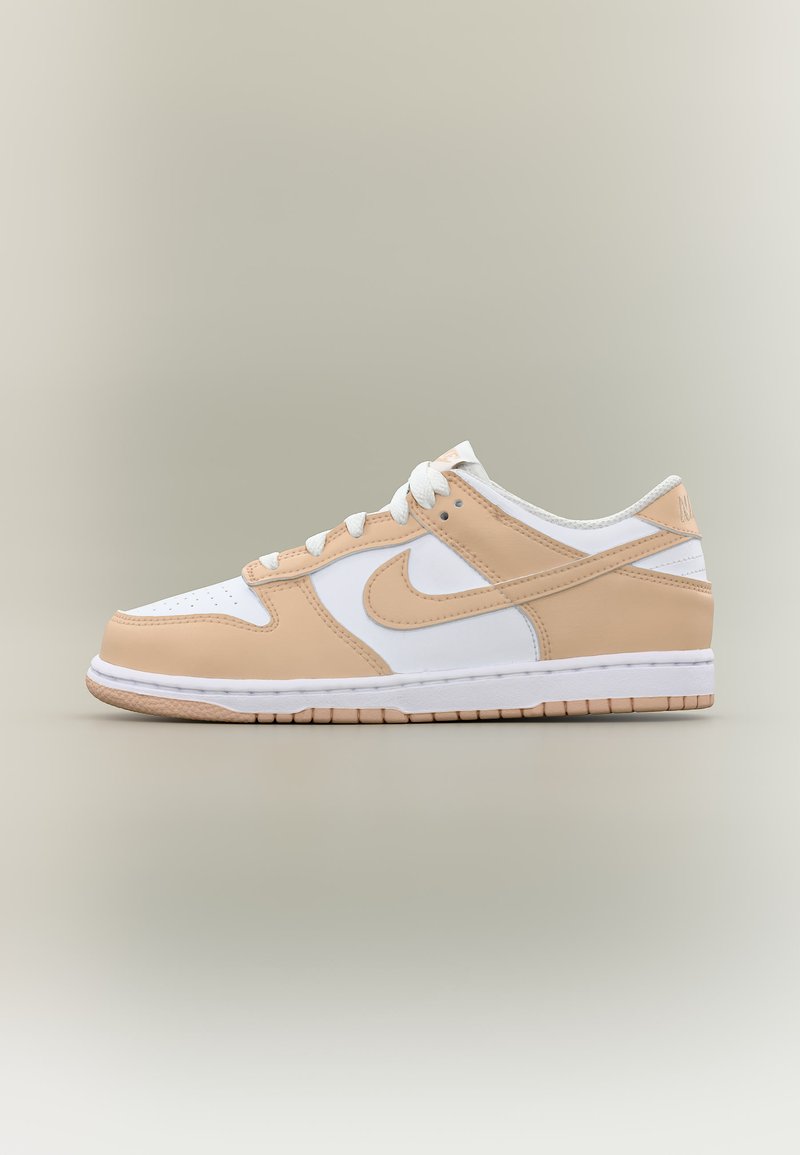Κοντό αθλητικό παπούτσι Nike με λευκά και μπεζ δερμάτινα πάνελ, λευκά κορδόνια και ελαστική σόλα σε ουδέτερο φόντο.