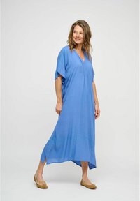 Bla dresses in knietiefe, mit kurzen Ärmeln, V-Ausschnitt und seitlichen Schlitzen. Leichtes Gewebe mit glatter Textur. Kombiniert mit hellbraunen Ballerinas.