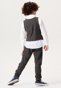 Grau gestreifte Weste über einem weißen Hemd, kombiniert mit grauen Hosen und blauen Turnschuhen. Sichtbare Struktur des Stoffes und taillierte Passform.