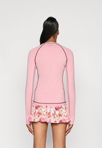 Top roz cu mâneci lungi, având cusături maro contrastante, asortat cu o fustă mini cu un model floral, cu tiv ondulat.