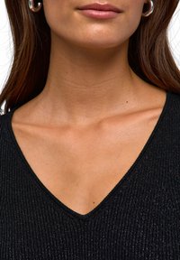 Top nero a costine con scollatura a V profonda, caratterizzato da un leggero luccichio. Primo piano della scollatura e dell'area della clavicola, evidenziando la texture e il design.