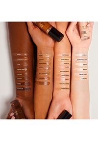 Three arms display foundation swatches in various skin tones, labeled with names. A concealer tube is held in the center.