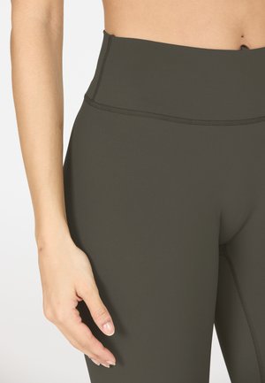 Leggings taille haute, vert foncé, en tissu lisse et extensible. Ils présentent des coutures plates et un ajustement serré autour de la taille et des cuisses.