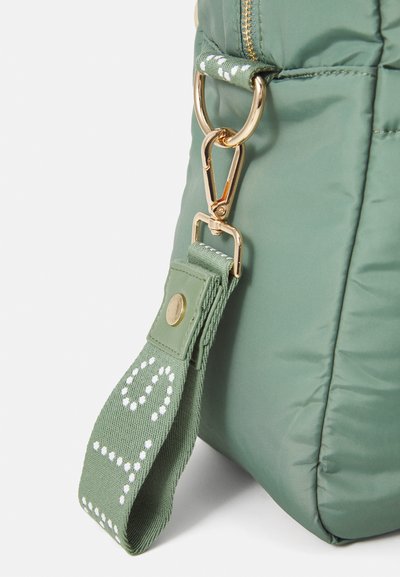 Geantă verde căptușită, dotată cu un clips din material metalic auriu și un bandou texturat cu modele punctate alb. Suprafață netedă cu un design minimalist.
