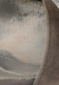 Gros plan de l'intérieur usé d'une chaussure en daim beige montrant des marques d'éraflures foncées et des coutures le long du bord supérieur.