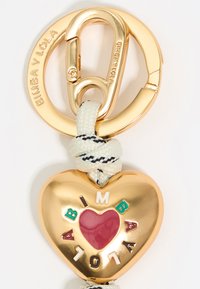 Llavero dorado con forma de corazón, con letras coloridas que forman la palabra "BIMBA," rodeado de un corazón rojo, y sujeto a una cuerda trenzada en blanco y negro.
