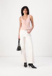 Light pink ribbed tank top with button detail, paired with white flared jeans. Black high-heeled boots and a small black handbag complete the look.