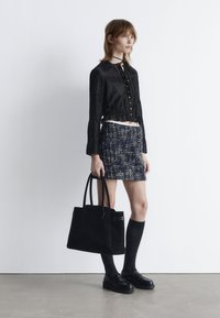 Black cropped blouse with buttons, textured navy tweed mini skirt, black suede tote bag, and knee-high socks with black loafers.