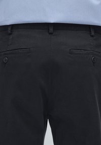 Black trousers with a smooth texture, featuring two rear pockets with button closures. Waistband designed for a tailored fit.