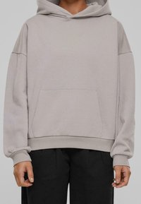 Sweat à capuche gris clair en tissu doux, avec une poche kangourou à l'avant, une coupe oversize, et des poignets et un ourlet côtelés.