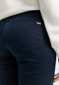 Navyblaue, taillierte Jeans mit glatter Textur, ausgestattet mit einer Gesäßtasche mit einem Etikett und dezenten Nähdetails.