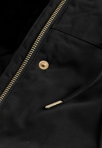 Sort lynlåset jakke med ribbet tekstur, der har en gylden lynlås og trykknaplukning. Kendt for sit holdbare stof og slanke design.