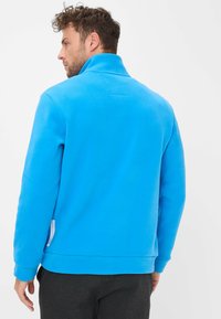 Giacca in pile blu con colletto alto, polsini e orlo a coste. Presenta un'etichetta sul lato sinistro e una texture liscia e morbida.