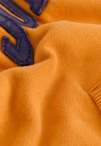 Primer plano de una suave tela naranja con detalles de letras bordadas en azul marino y textura y pliegues visibles.