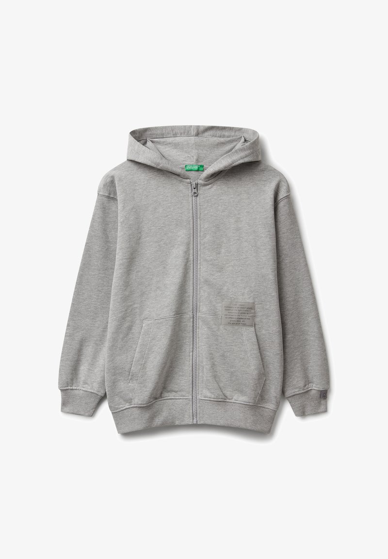 Felpa grigia chiara con zip, dotata di tasche frontali, cappuccio, polsini a coste e una piccola toppa rettangolare sul lato destro in basso.