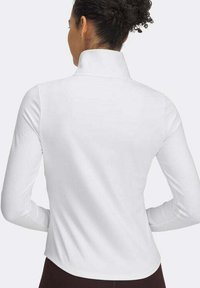 Fehér, hosszú ujjú felső magas gallérral, sima textúrával és testhez simuló fazonnal. A hátulról készült képen kiemelkedik a ívelt szegély és a varrat nélküli kivitelezés.