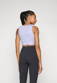 Paarse sportbeha met het Nike Pro-logo op de band, gecombineerd met zwarte high-waisted legging. Glad, rekbaar materiaal, mouwloos ontwerp.