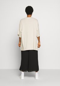 Overmatig grote beige t-shirt met korte mouwen, gecombineerd met zwarte geplooide wijde broek, met witte sneakers en enkel-sokken.