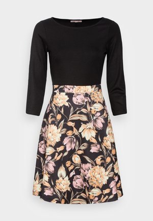 Vestido negro con mangas tres cuartos y una falda acampanada con un patrón floral en tonos melocotón y rosa sobre un fondo oscuro.