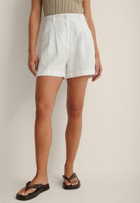 Hvide linnedshorts med høj talje, læg og opkrøllede nederkanter. Båret med mørke flip-flops. Struktureret og let stof.