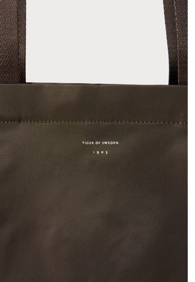 Barna vászontáska vastag, sötét pántokkal. A varrás felett fehér színű "TIGER OF SWEDEN 1903" felirat található. Simább textúra.
