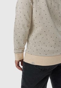 Felpa color beige chiaro con piccoli motivi multicolori, polsini a coste e orlo in beige chiaro a contrasto. Il tessuto è texturizzato e informale.