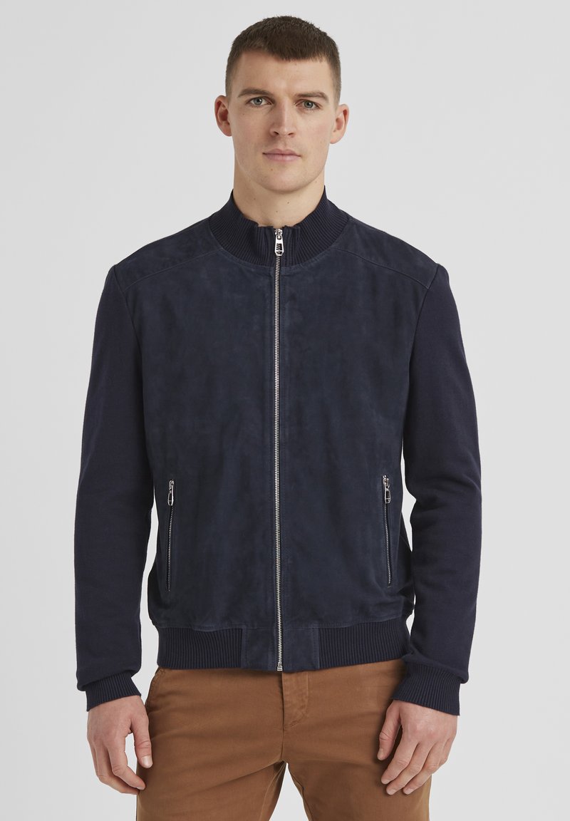 Marineblaue Bomberjacke mit einer glatten Wildlederfront, geripptem Strickkragen und -bündchen, zwei seitlichen Reißverschlüssen und einem taillierten Saum.