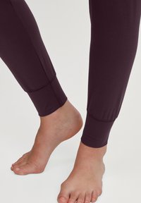Donkerviolet leggings met een gladde textuur, een aansluitende pasvorm en elastische boorden bij de enkels. Naaddetails zijn zichtbaar langs de zijkanten.