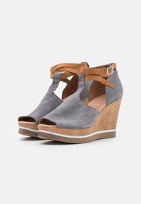 Sandales compensées en daim gris avec bout ouvert, semelle intermédiaire semblable au liège et brides à la cheville en cuir tan avec boucle. Texture lisse avec accents contrastants.