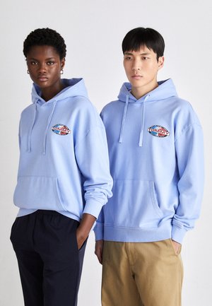 Sudadera de algodón azul con un bolsillo frontal, que presenta un logo en el pecho. La tela parece suave y lisa, con un corte holgado.