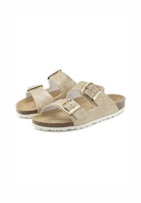 Beige slide sandals with two adjustable straps and gold metal buckles, featuring a textured footbed and white rubber outsole.