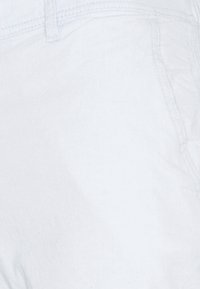 Detailní záběr na bílou denimu, ukazující švy kapsy a poutka na opasek.