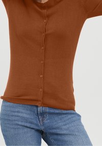 Brun stickad cardigan med knappstängning, ribbat nederkant och långa ärmar, tillsammans med ljusblå jeans. Slät textur, figursydd design.
