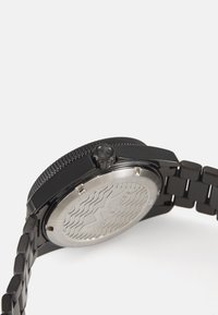 Reloj de pulsera de metal negro con una tapa trasera texturizada, una corona con un acento negro y un diseño de pulsera con eslabones. Acabado suave y elegante.