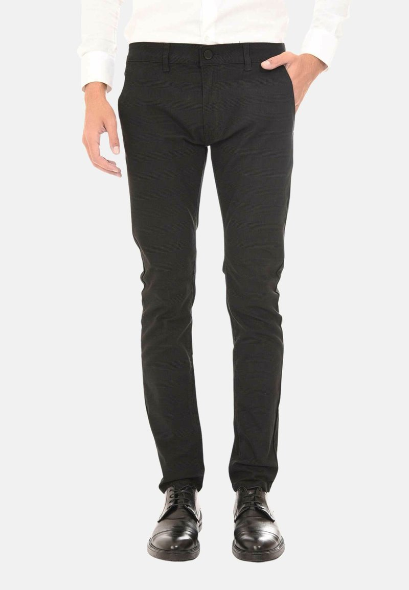 Pantaloni chino neri con una vestibilità slim, realizzati in cotone, caratterizzati da una texture liscia, passanti per cintura e tasche frontali, abbinati a scarpe eleganti nere.