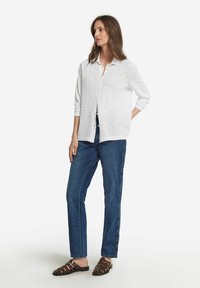 Vit långärmad skjort cardigan med knappar, parat med blå raka jeans och bruna sandaler med remmar. Mjukt tyg, avslappnad passform, minimalistisk design.