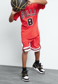 Czerwona koszulka do koszykówki z napisem "BULLS" i numerem "8", w zestawie z dopasowanymi czerwonymi szortami. Czarno-złote sneakersy Nike z błyszczącymi akcentami.