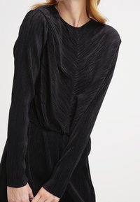 Top negro de manga larga con textura acanalada vertical, que presenta una silueta ajustada y cuello redondo, diseñado para una apariencia elegante.