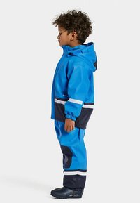 Blue waterproof jacket and pants with black and white accents. Features hood, elastic cuffs, and rubber boots. Smooth, durable material.