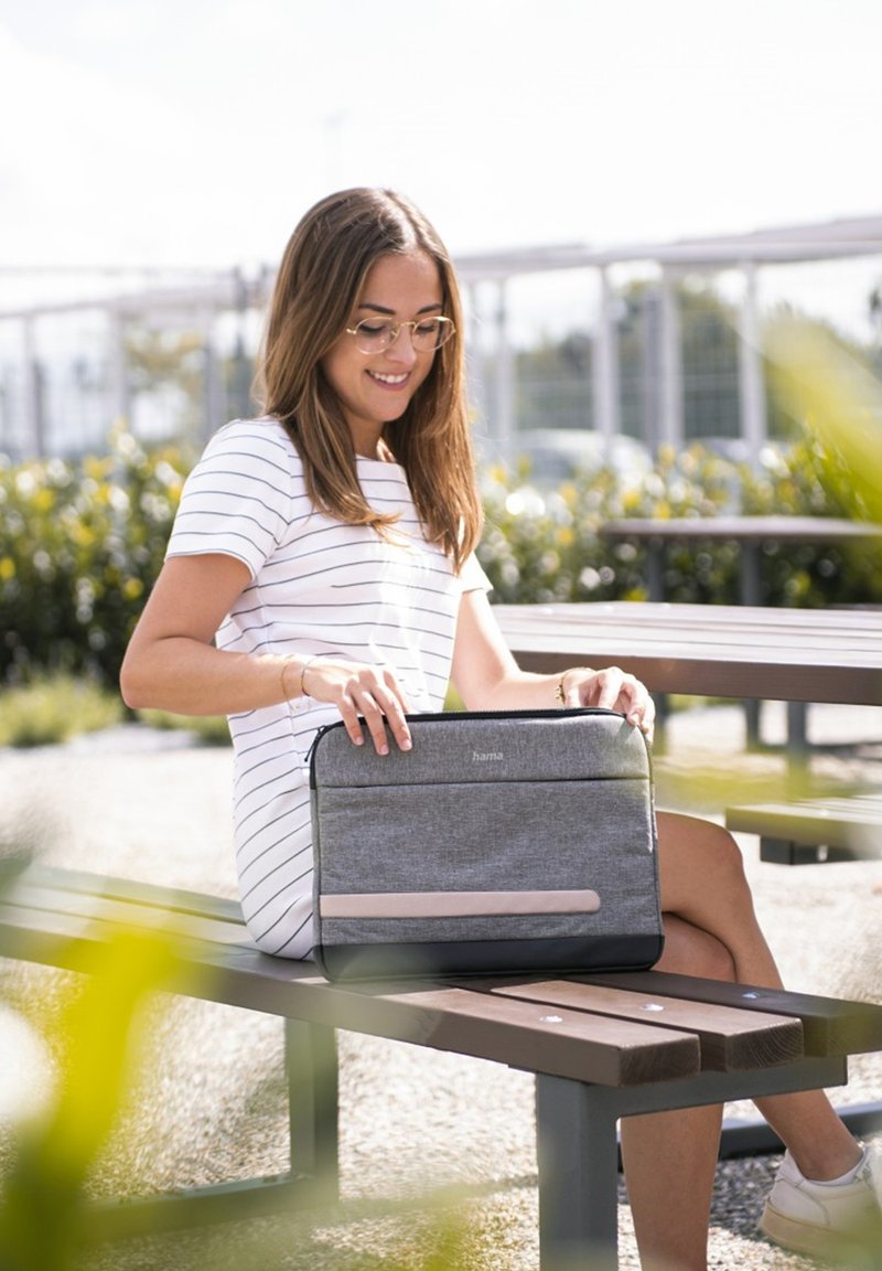 Grau gefütterte Laptop-Hülle mit einem hellrosa Akzent, mit Reißverschluss und schickem Design. Auf einer Holzbänken im Freien platziert.