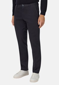 Zili tumši zili kokvilnas zvīņi ar gludu tekstūru, ar pogu aizdari, sānu kabatām un pielāgotu piegriezumu, kombinēti ar baltām kedām.