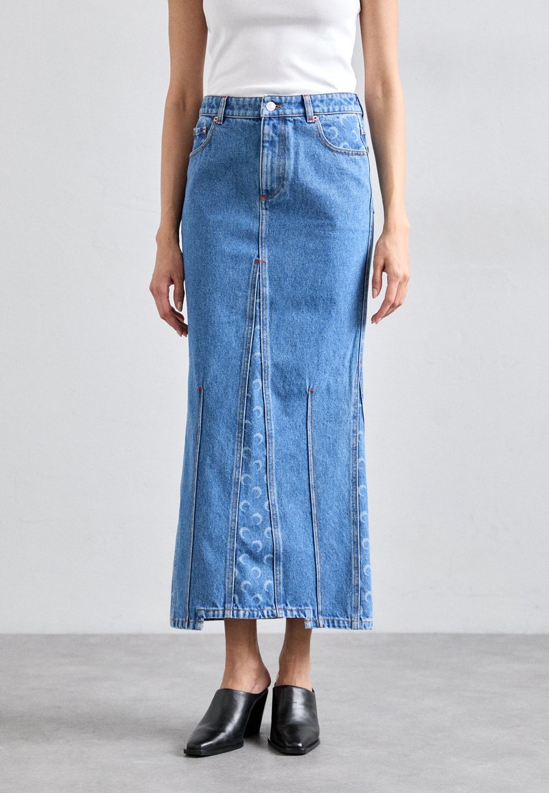 Denim maxi skirt with a straight cut, light blue color, prominent stitching, front slit, and decorative pattern along the hem. Black heeled mules.