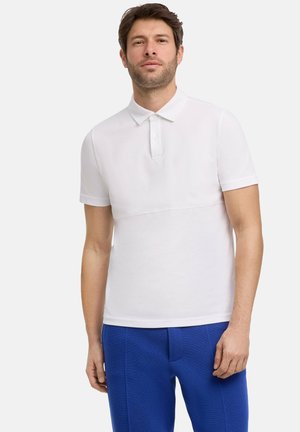 Weißes Poloshirt mit kurzen Ärmeln, geknöpftem Kragen und gerippter Textur, kombiniert mit blauen Hosen im eleganten, figurbetonten Design.