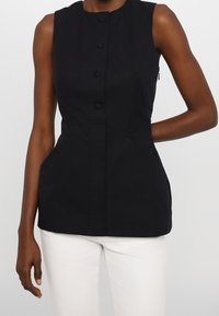 Svart ärmlös topp med rund halsringning, fem knappar framtill och sidofickor; skräddarsydd passform med ett slätt, strukturerat tyg.