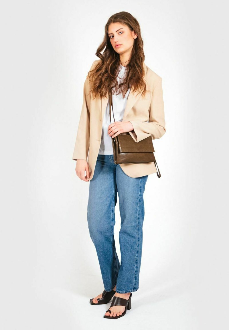 Blazer beige sopra una maglietta bianca, jeans azzurri chiari e sandali neri con tacco. Porta una borsa a tracolla piccola di colore marrone scuro con chiusura a pattina.