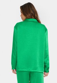 Emerald green satin shirt with a relaxed fit, long sleeves, and a collar. Smooth texture with minimal shine and a straight hem.
