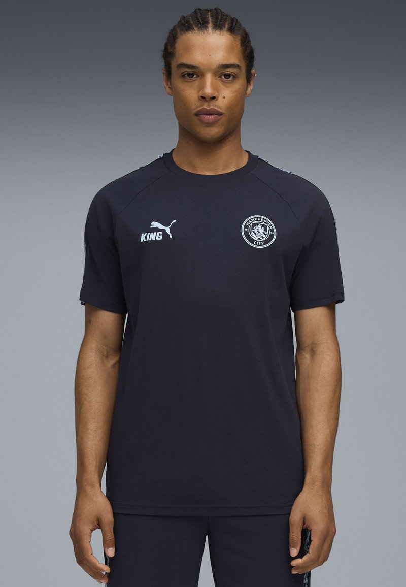 Kortærmet marineblå sportsskjorte lavet af blødt stof, med hvidt logo og detaljer, rund halsudskæring og løs pasform.