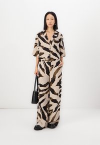 Ensemble deux pièces imprimé animal beige et noir comprenant une chemise à manches courtes à boutons et un pantalon large, accessoirisé d'un sac à main noir.