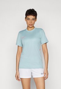 Vaaleansininen lyhythihainen urheilupaita, jossa on pyöreä kaula-aukko ja vaaleanpunainen Nike-logo rinnassa. Yhdistetty valkoisiin urheilushortseihin.