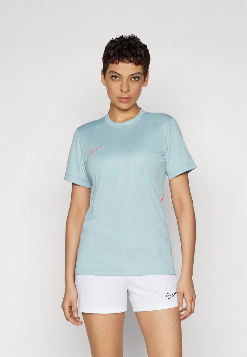 Vaaleansininen lyhythihainen urheilupaita, jossa on pyöreä kaula-aukko ja vaaleanpunainen Nike-logo rinnassa. Yhdistetty valkoisiin urheilushortseihin.